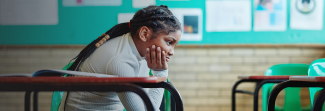 Girl by herself in school classroom deep in thought.