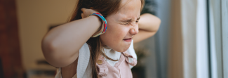 Child being stressed and blocking her ears with her hands.