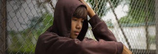 Teen sitting up against a fence thinking about something.